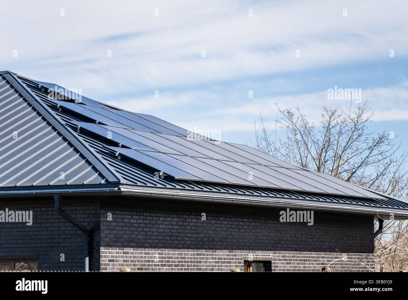 I moderni pannelli fotovoltaici sono installati su un tetto di cuciture in metallo grigio scuro di una casa privata in mattoni che mostra soluzioni di energia rinnovabile per sus Foto Stock