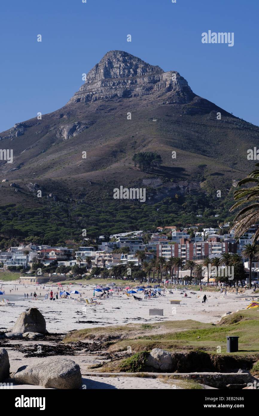 Giornata tipica in spiaggia a Camps Bay, città del Capo, Sud Africa. La testa di Leone sullo sfondo, contro un cielo blu. Foto Stock