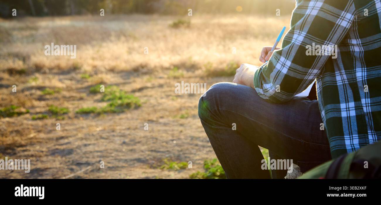 Uomo che scrive su un notebook all'aperto durante l'ispirazione del tramonto Foto Stock