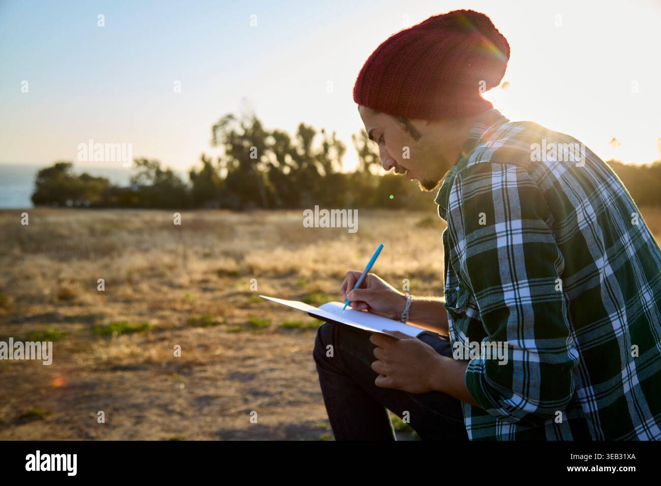 Uomo che disegna sul diario all'aperto al tramonto Foto Stock