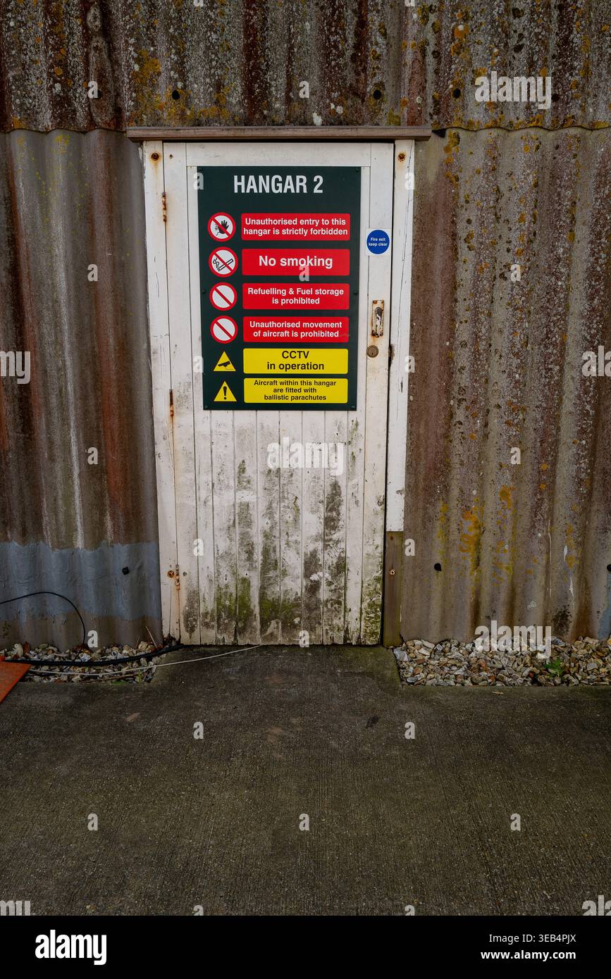 Aprile 2026 - porta invecchiata con cartelli segnaletici per l'Hanger 2 sul circuito Goodwood Race, West Sussex, Inghilterra, Regno Unito. Foto Stock