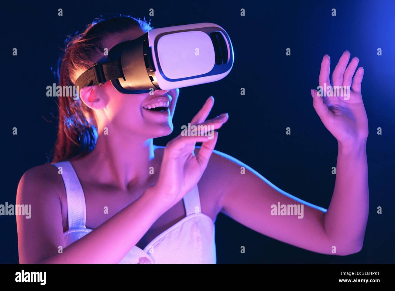 Una donna coinvolgente sperimenta la realtà virtuale in un ambiente vivace con l'illuminazione dinamica Foto Stock