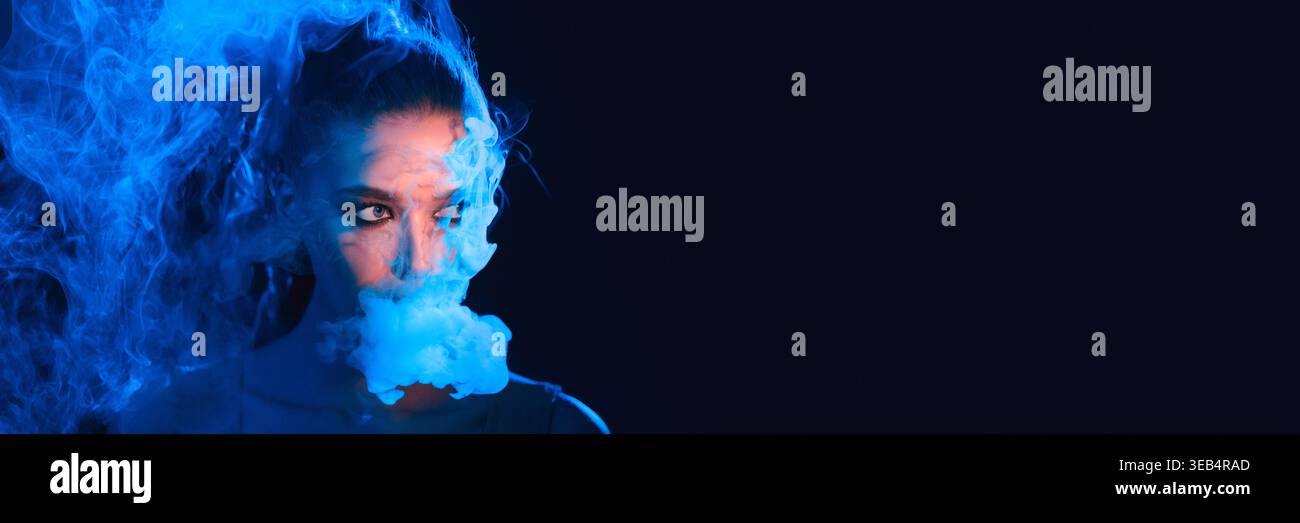 Donna circondata dal fumo blu in un ambiente buio durante una sessione artistica creativa Foto Stock