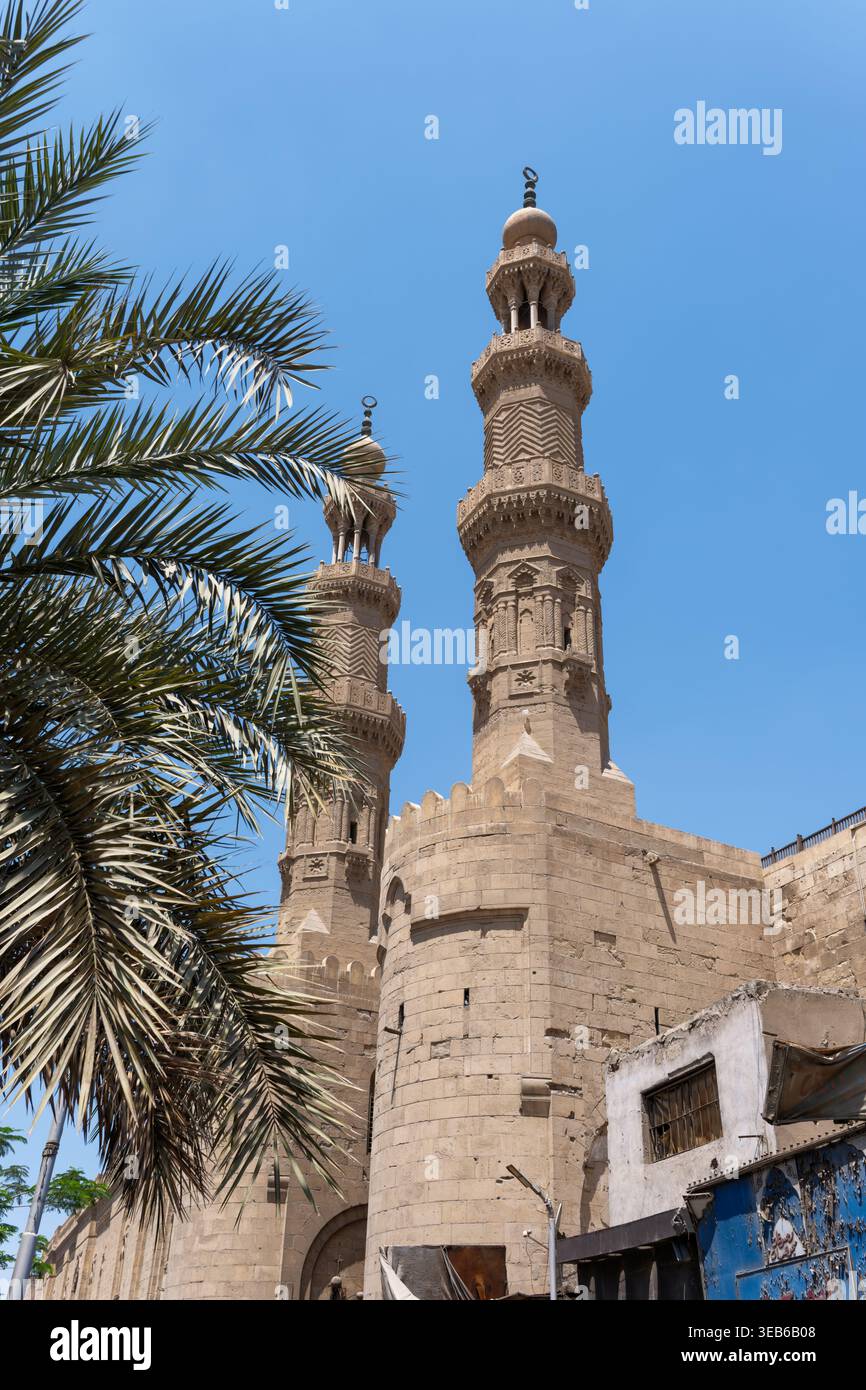 Vista di Bab Zuwayla con i suoi due torreggianti minareti ornati e le fronde di palme sotto un cielo azzurro limpido a El-DARB El-Ahmar, Governatorato del Cairo, Egitto. Foto Stock