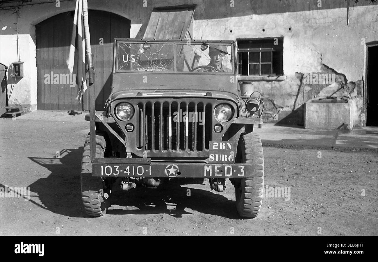 Una Jeep medica dell'esercito degli Stati Uniti del 410th Infantry Regiment della 103rd Infantry Division, marchiata per la sezione chirurgica del 2nd Battalion, parcheggiata accanto ad un edificio in quella che è probabilmente l'Alsazia, Francia, tra la fine del 1944 e l'inizio del 1945. I codici del parabrezza e del paraurti incrinati riflettono la campagna invernale della divisione. Foto Stock