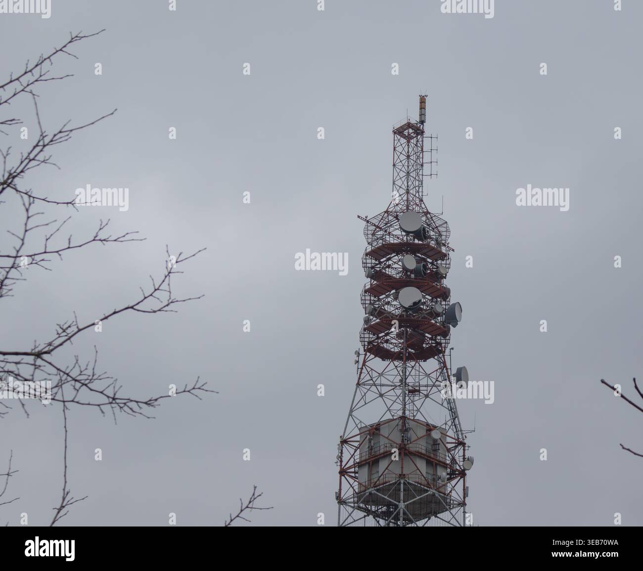 Torre di telecomunicazione a reticolo in acciaio con parabole satellitari e antenna contro un cielo coperto di colore grigio Foto Stock