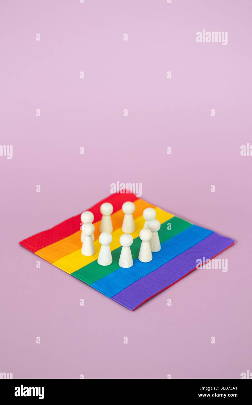 Un gruppo di statuette di legno si erge in cerchio sulla bandiera arcobaleno con sfondo rosa. DEI Diversity, Equity, and Inclusion policy Implementation Foto Stock