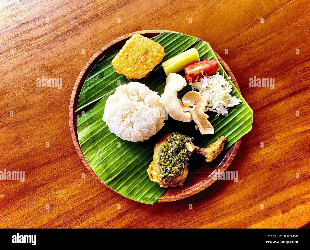 Vista dall'alto del cibo indonesiano, Ayam Penyet o Ayam geprek, pollo fritto con salsa al peperoncino verde (sambal) con riso e verdure, su foglia di banana - Immagine stock catturata con smartphone