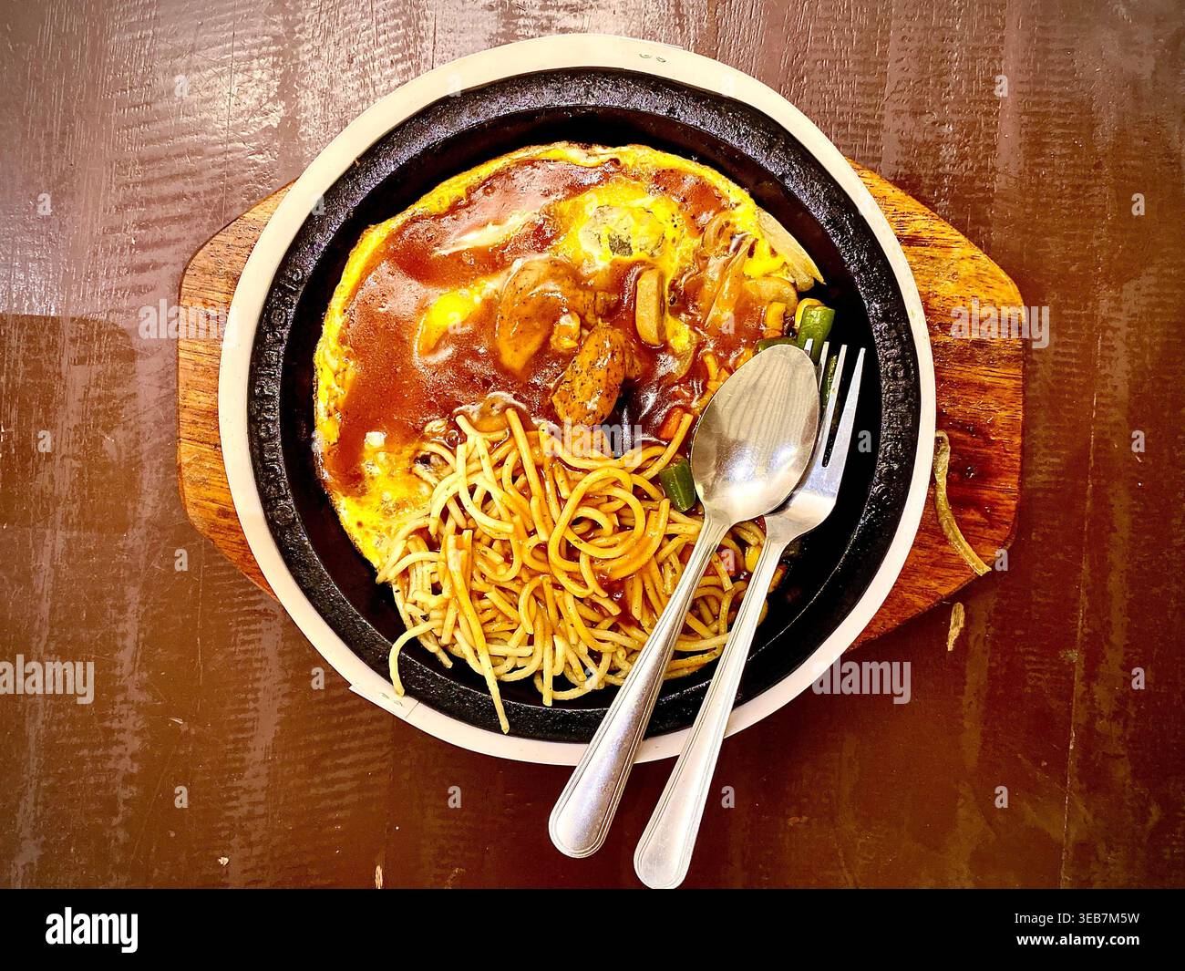 Foto della cucina di un delizioso tritatutto di pollo al peperoncino nero sfrigolante con tagliatelle e Sunny Side Up (uova fritte) servito su una piastra calda di ferro nero - Immagine stock catturata con smartphone