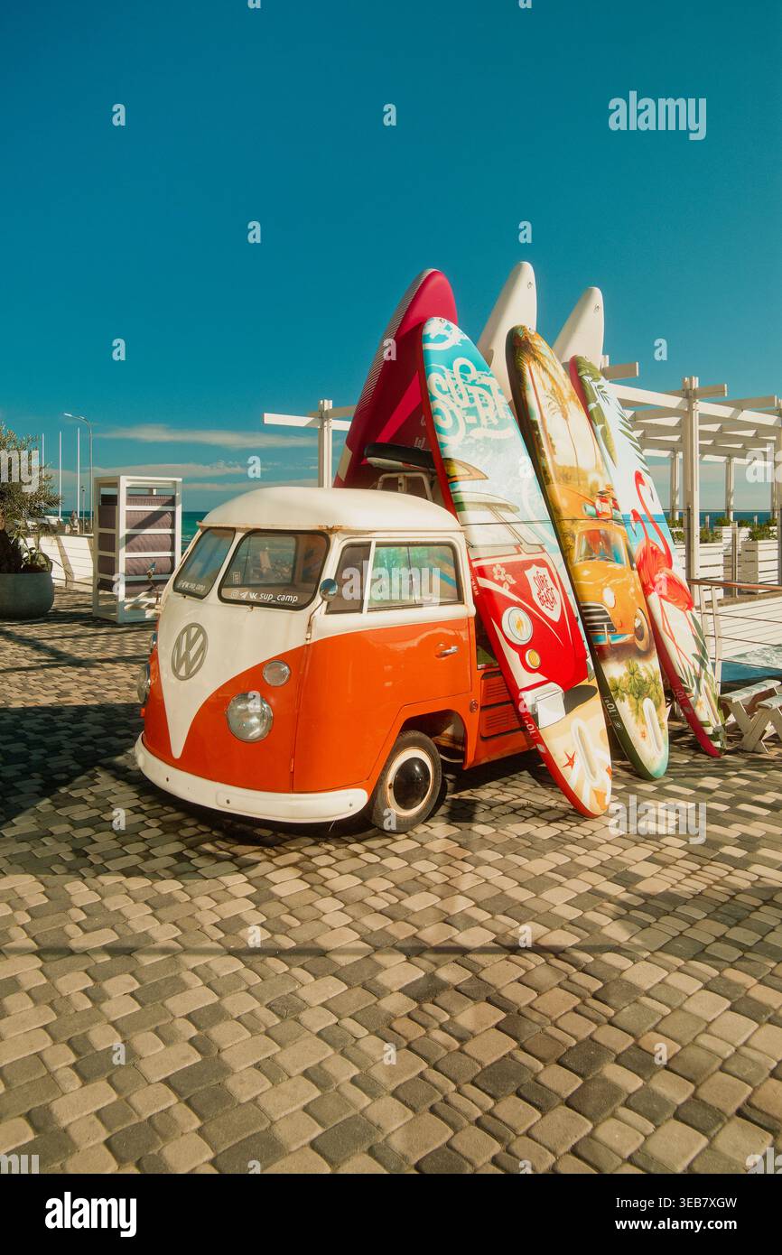 Ambiente nostalgico sul lungomare che presenta tavole da surf retro con pavimentazione in ciottoli illuminata dal sole e cielo azzurro Foto Stock