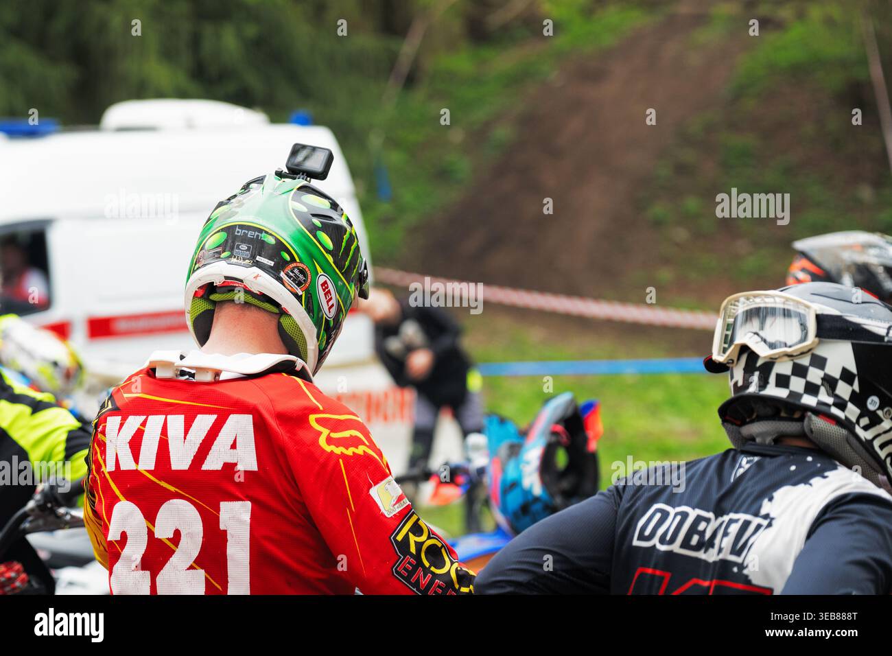 VLADIKAVKAZ, RUSSIA - 18 APRILE 2026: Piloti Enduro con action camera sui caschi preparati per la gara con un'ambulanza sullo sfondo Foto Stock