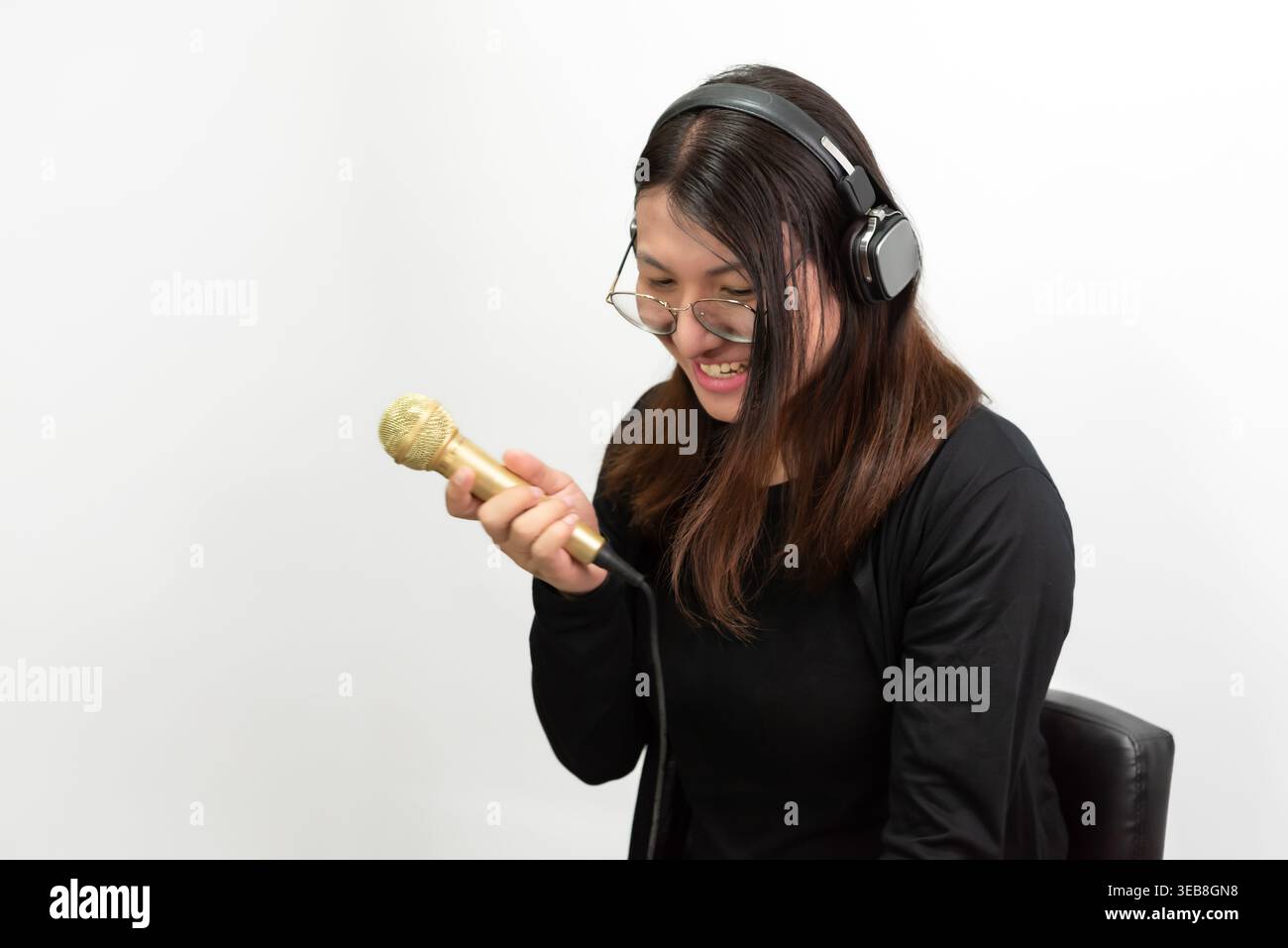 Donna asiatica LGBTQ sicura di sé che indossa le cuffie che canta con microfono in studio sfondo minimale espressione gioiosa musica creativa stile di vita e sel Foto Stock