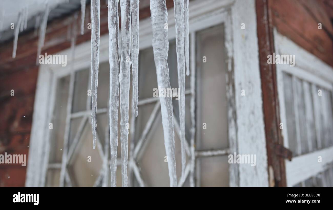 Ghiaccioli appesi alle grondaie della vecchia casa durante la stagione invernale fredda e nevosa Foto Stock