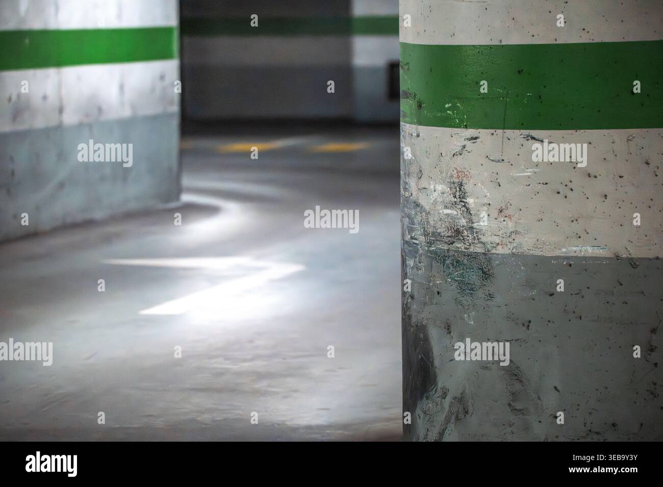 Vista di un pilastro di cemento graffiato con una striscia verde in un garage sotterraneo vuoto con frecce dipinte sul pavimento. Foto Stock