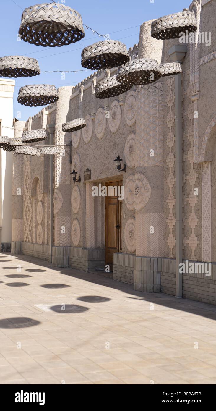 Vista di una facciata tradizionale di un edificio con intricati rilievi geometrici e cesti in tessuto appesi su un passaggio pedonale lastricato a Tashkent, Uzbekistan. Foto Stock