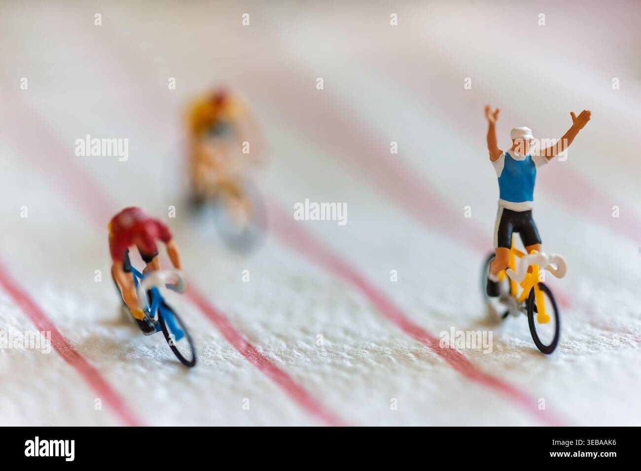 Piccoli ciclisti modellini corrono su una superficie a righe, con il leader che alza le braccia in vittoria per simboleggiare il raggiungimento di traguardi commerciali e finanziari Foto Stock