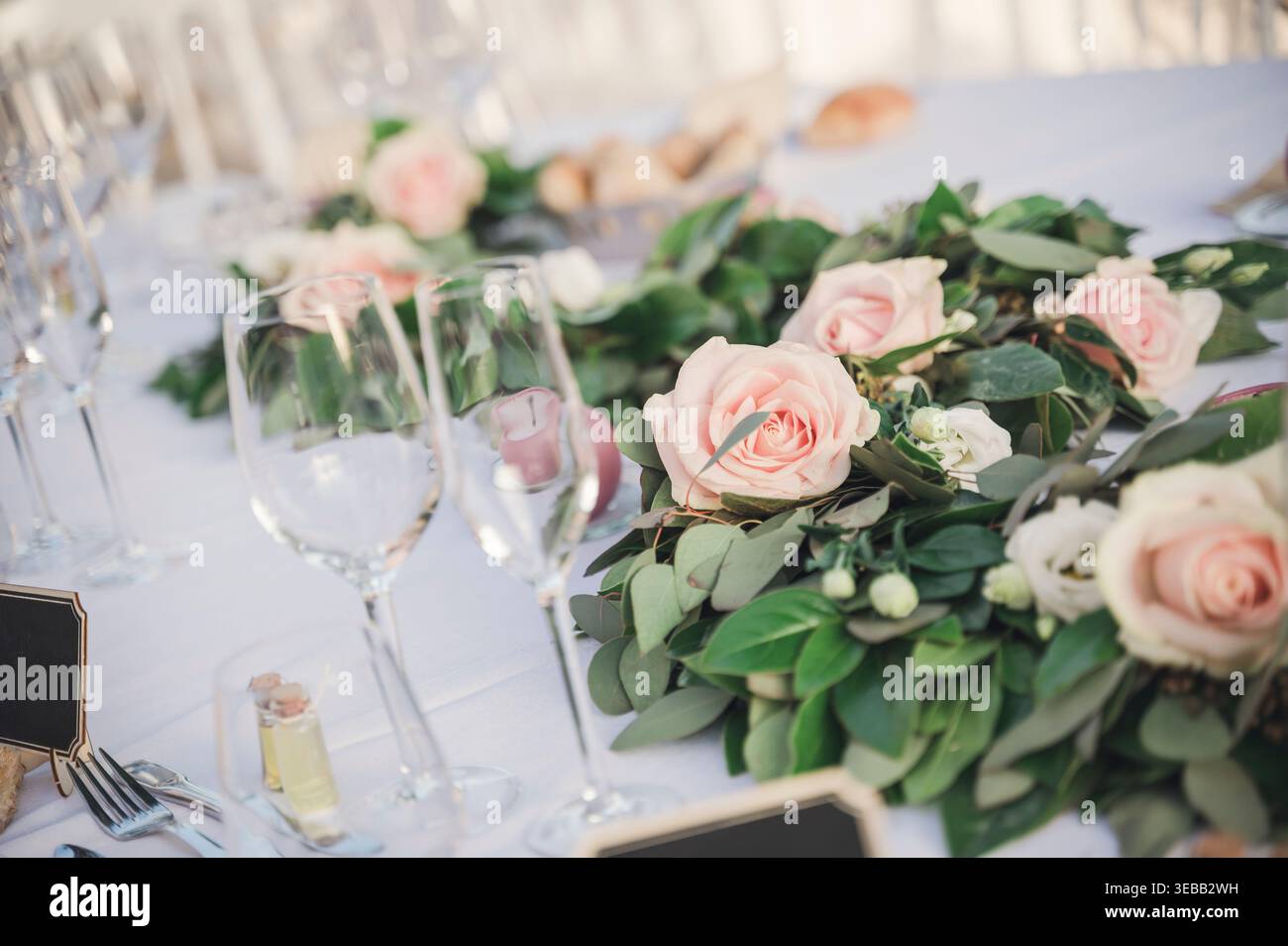 Sofisticato tavolo per ricevimenti nuziali con rose rosa, verde e cristalleria. Foto Stock