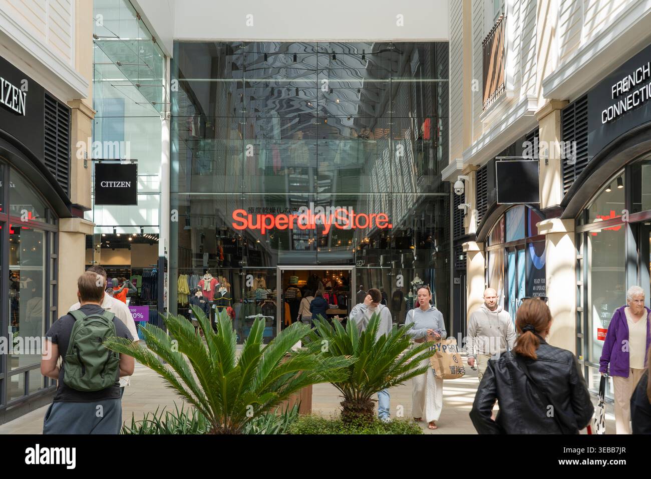 Gli amanti dello shopping e i visitatori del centro commerciale outlet Gunwharf Quays con un negozio Superdry alle spalle, Portsmouth, Regno Unito. Un marchio di moda britannico fondato nel 2003 Foto Stock