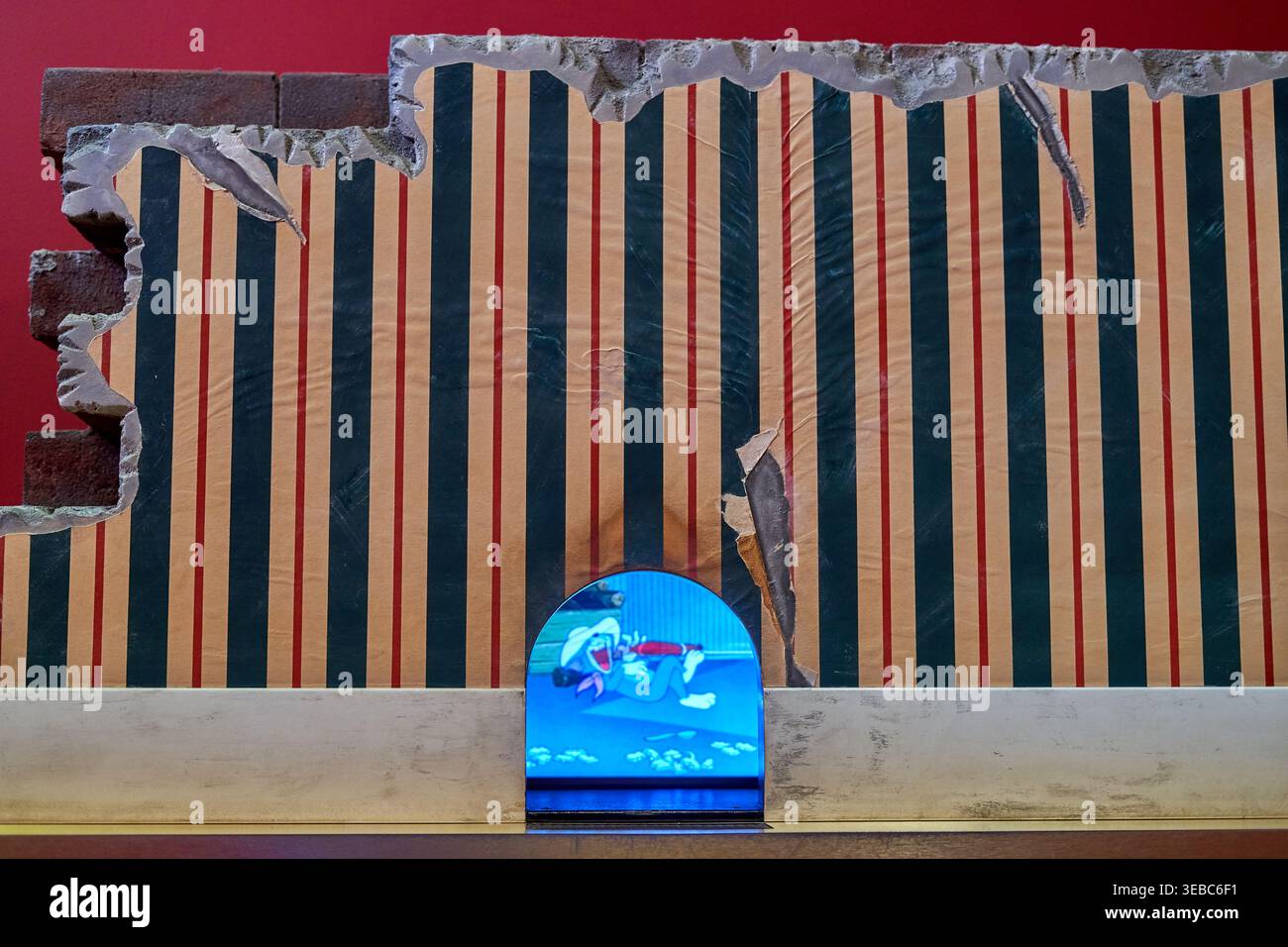 Una vista ravvicinata di un'installazione artistica con una parete su cui si stacca una carta da parati a righe in linee verticali crema, blu scuro e rosso. La carta da parati è Foto Stock
