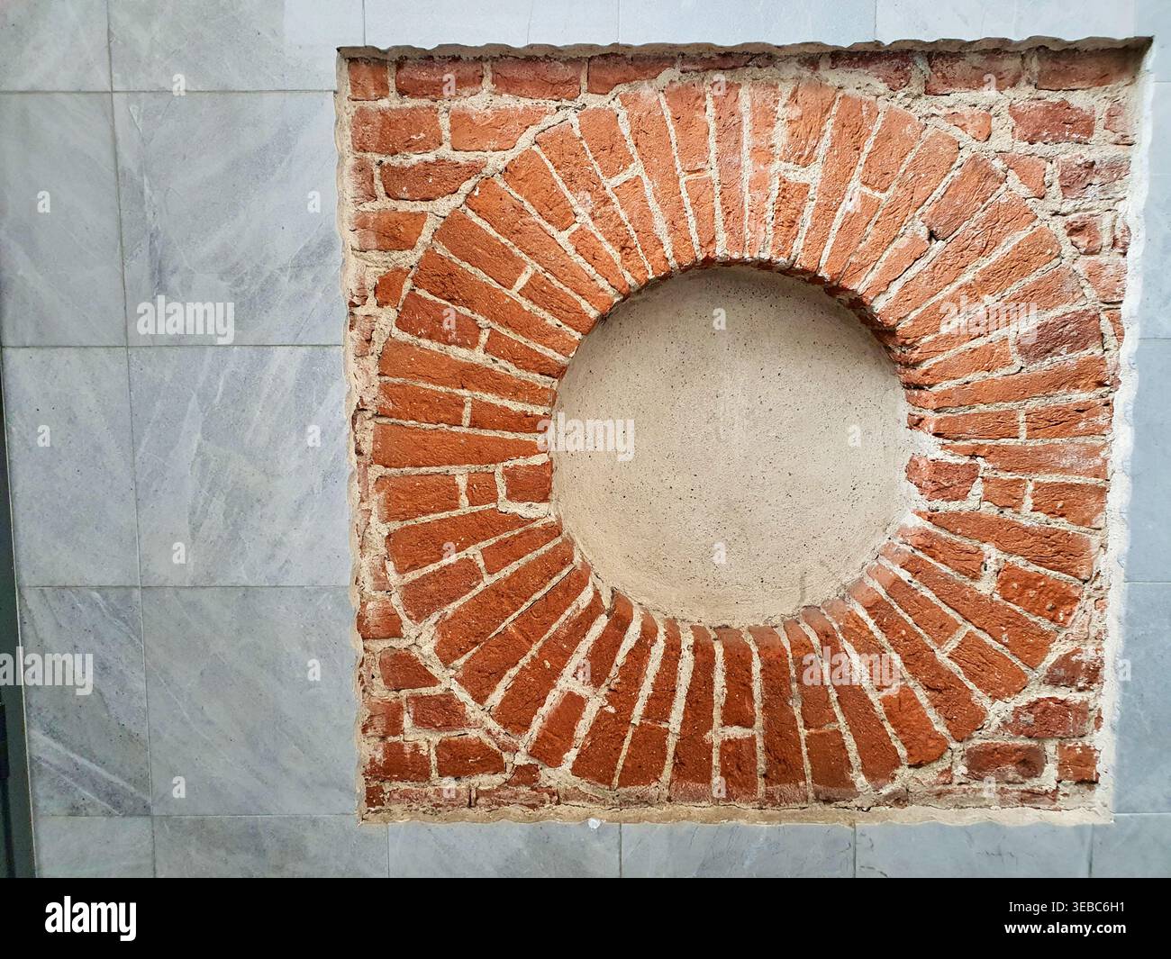 Un dettaglio architettonico in primo piano che mostra una sezione quadrata di mattoni rossi a vista inserita in una parete di piastrelle di marmo grigio. I mattoni sono disposti in un Foto Stock