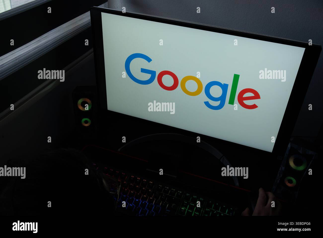 Il logo aziendale di Google multicolore viene visualizzato su un monitor del computer in un ambiente buio da ufficio domestico Foto Stock
