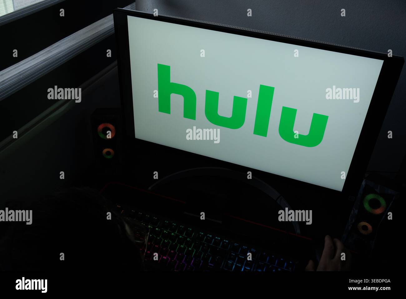 Il logo verde del servizio di streaming Hulu viene visualizzato sul monitor di un computer in un ambiente buio da ufficio domestico Foto Stock