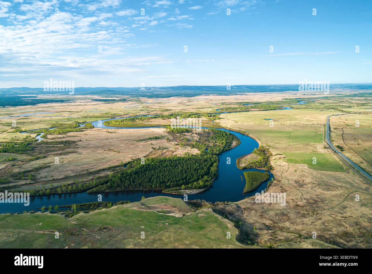 La vista panoramica di un tortuoso fiume scorre attraverso vaste praterie e foreste sotto un cielo primaverile limpido Foto Stock