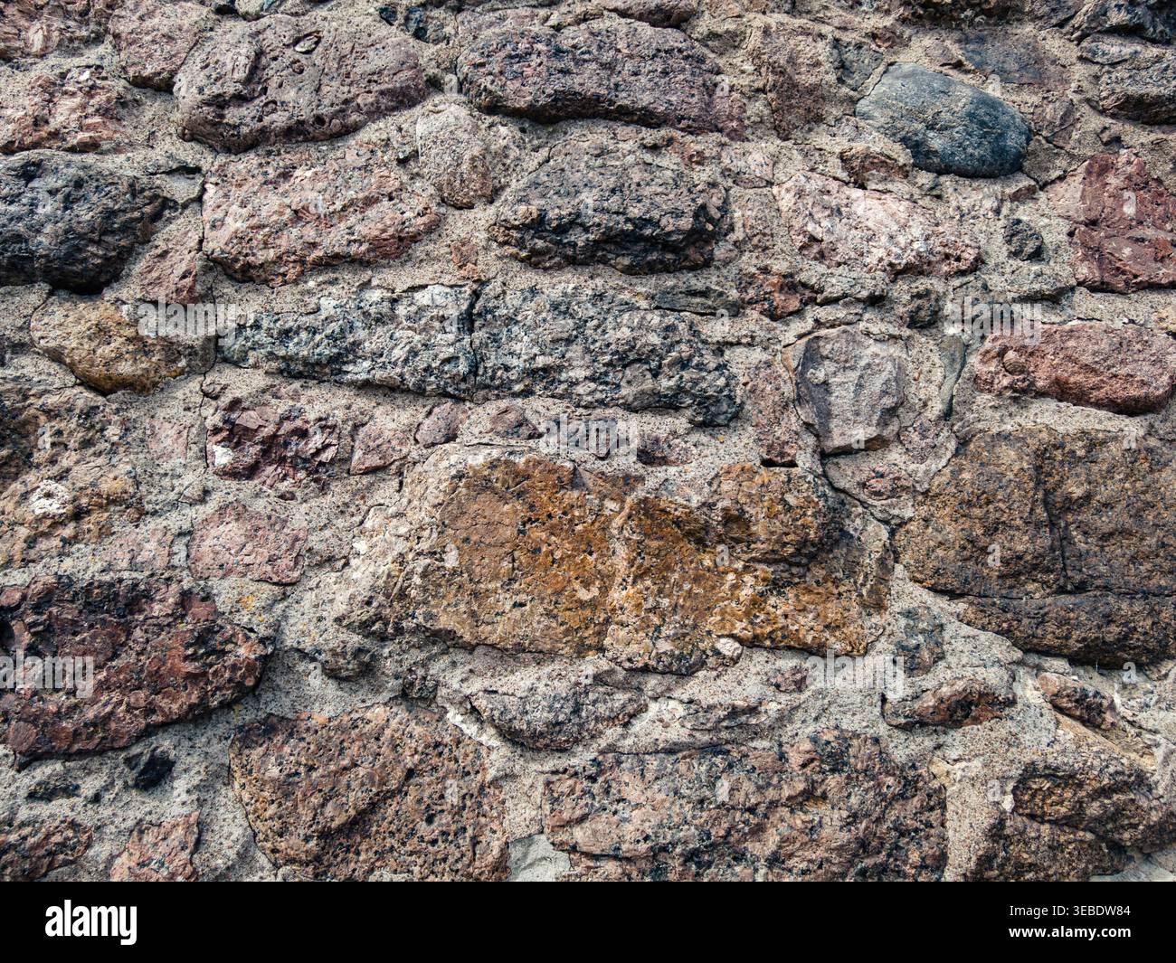 Ruvida consistenza di un antico muro di pietra che mostra vari colori naturali e Malta intemprata all'aperto Foto Stock