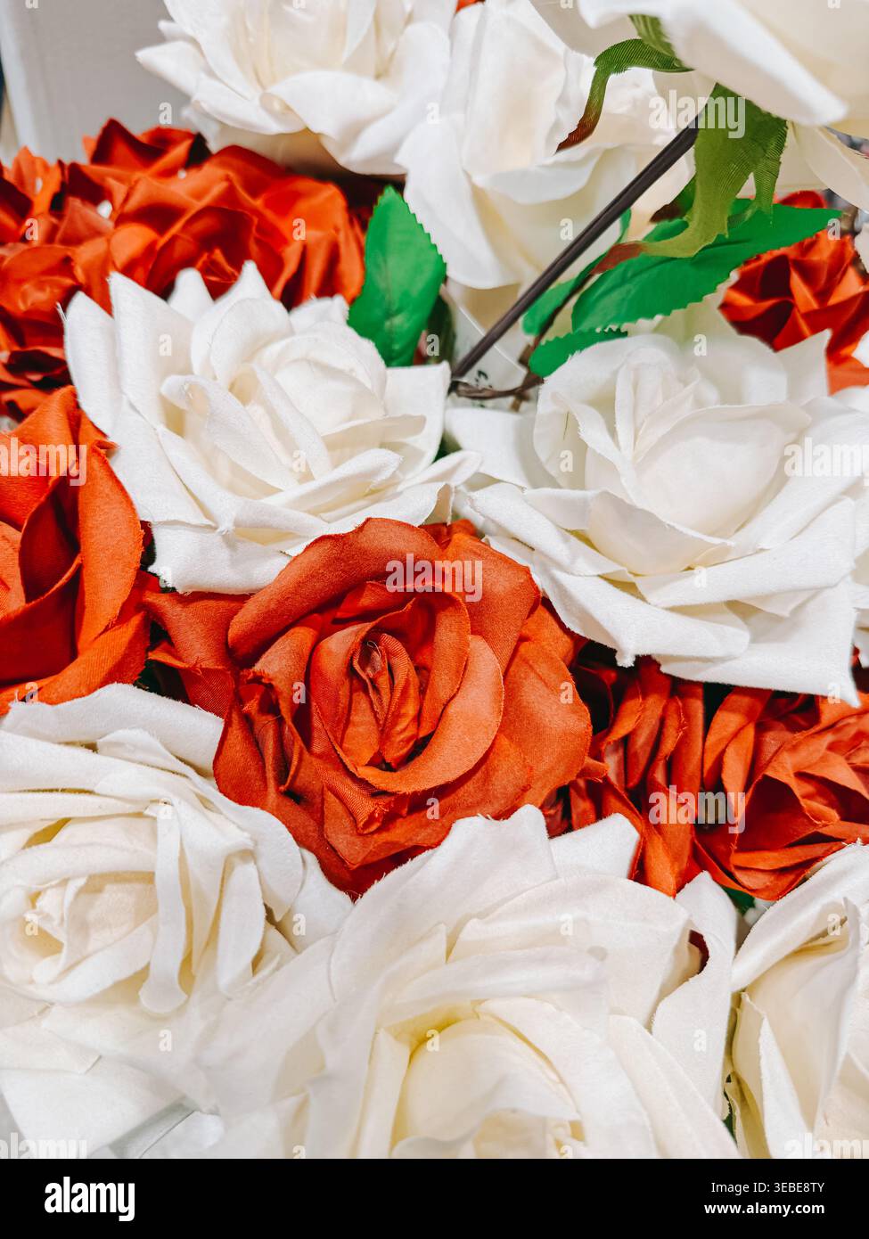 Primo piano dettagliato di rose artificiali rosse e bianche con petali di tessuto morbido e foglie verdi. Perfetto per sfondi floreali, temi romantici, matrimoni Foto Stock