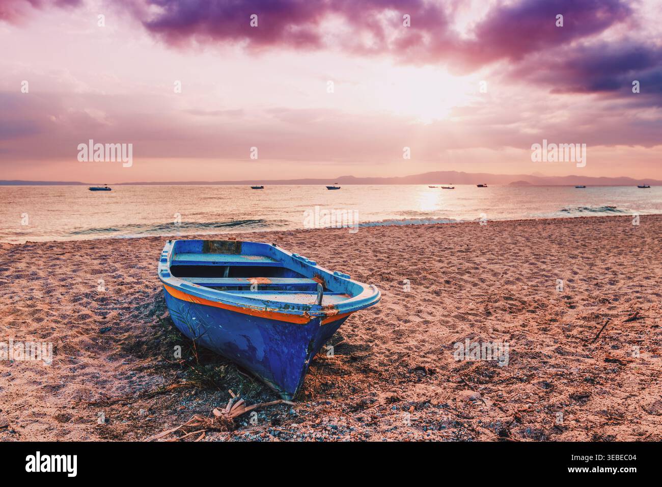 Una vecchia barca da pesca blu intemprata riposa su una spiaggia sabbiosa al tramonto. Il cielo è inondato di calde tonalità di rosa, viola e arancione, con nuvole sparse Foto Stock