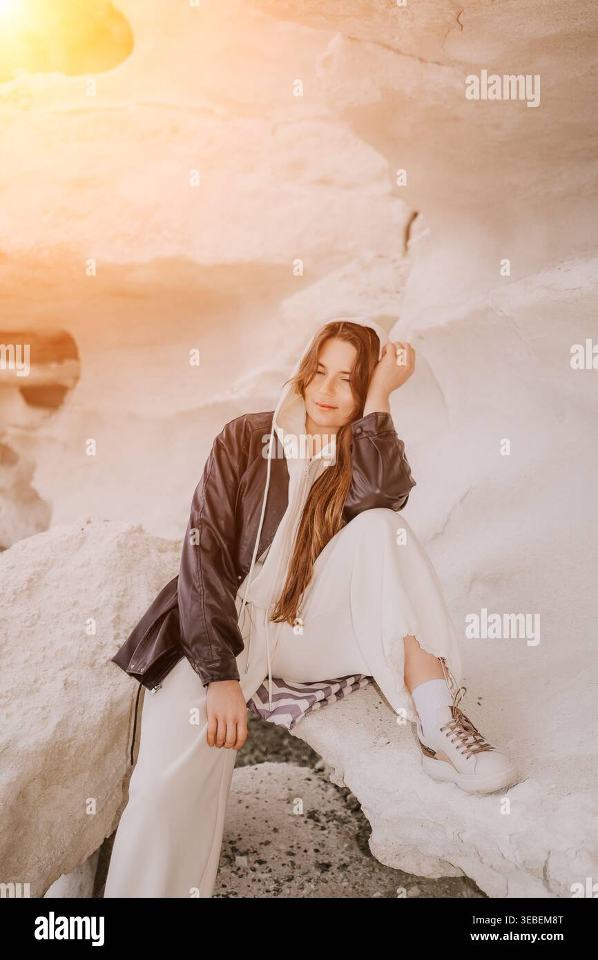 Donna seduta sulle scogliere il giovane viaggiatore in giacca di pelle si rilassa sulle formazioni di roccia bianca durante la luce dorata dell'ora Foto Stock