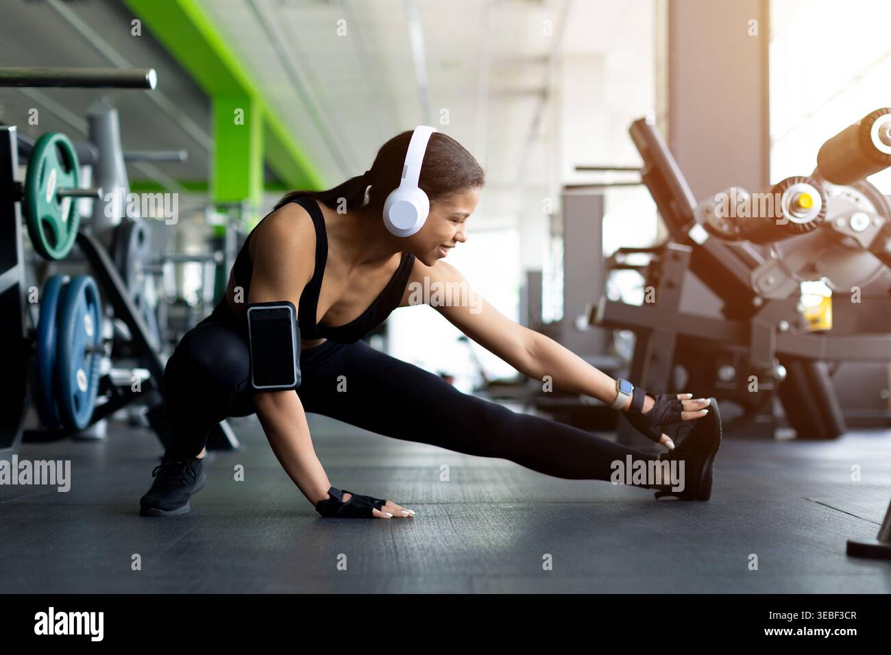 La giovane donna nera che fa un affondo laterale si allunga sul pavimento della palestra Foto Stock