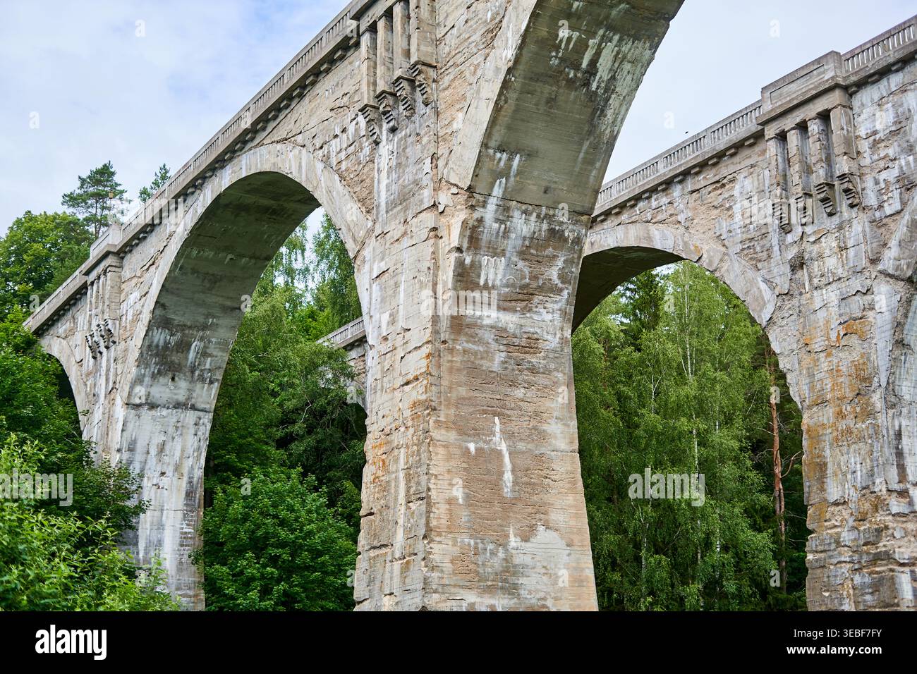 Vista ad angolo basso di un enorme viadotto ferroviario in pietra o cemento eroso, con più grandi archi, che mostra un'età significativa e una superficie consumata Foto Stock