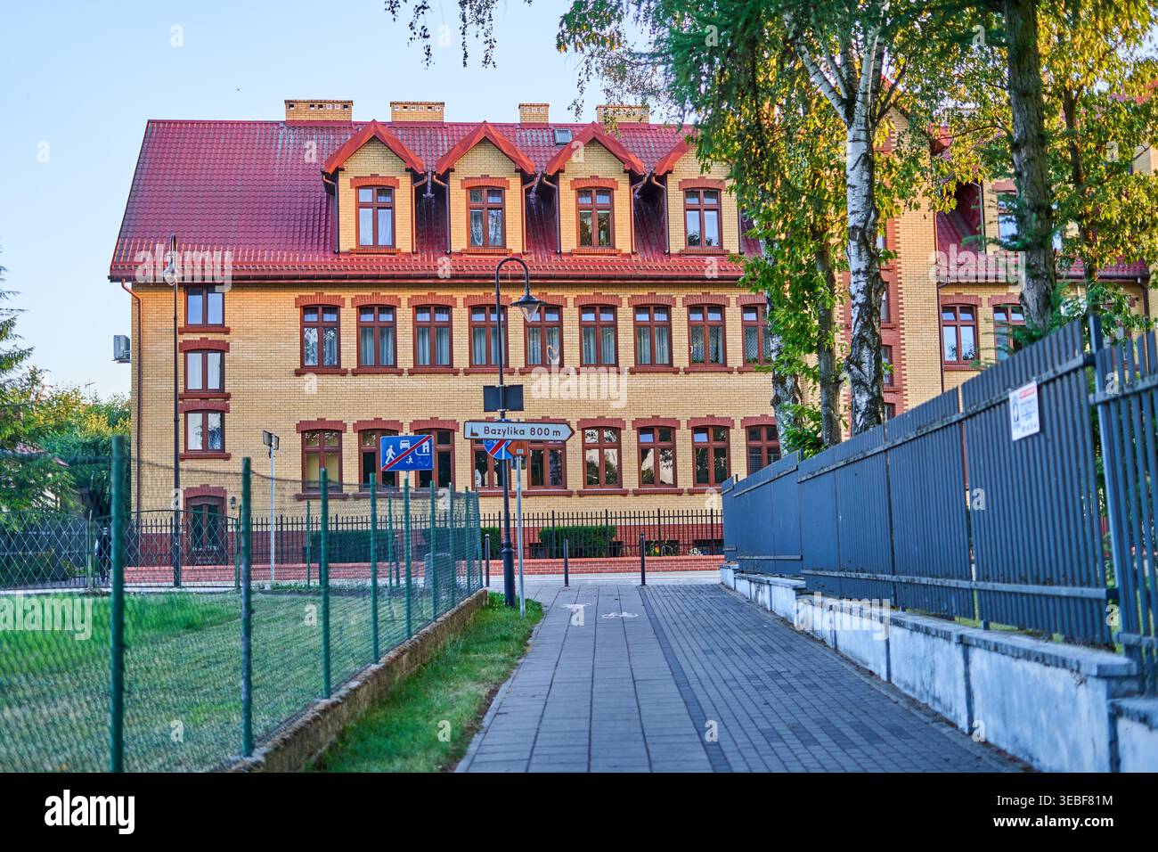 Un edificio storico in mattoni gialli a tre piani con tetto di tegole rosse e finestre a mansarda, visto da un marciapiede lastricato. L'architettura Foto Stock