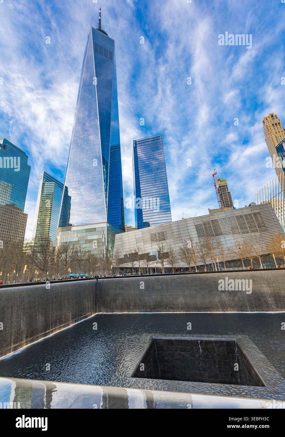 I visitatori esplorano la tranquilla National September 11 Memorial Plaza, riflettendo sul passato, mentre un World Trade Center svetta sopra lo sfondo. Foto Stock