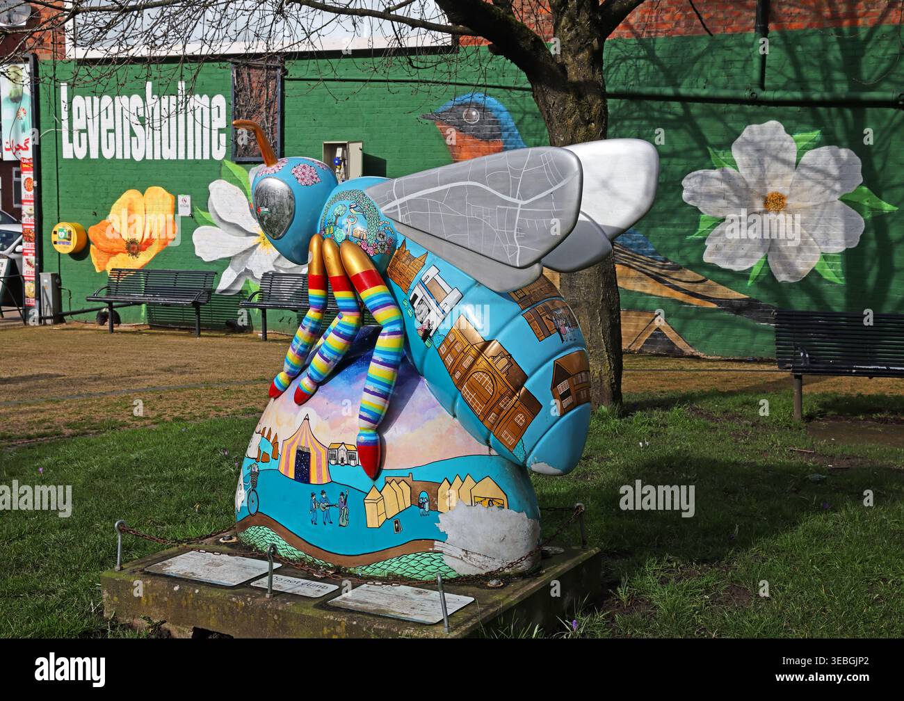 Levenshulme Village Green Bee in the City scultura con sfondo murale, arte pubblica della comunità di Greater Manchester. Foto Stock