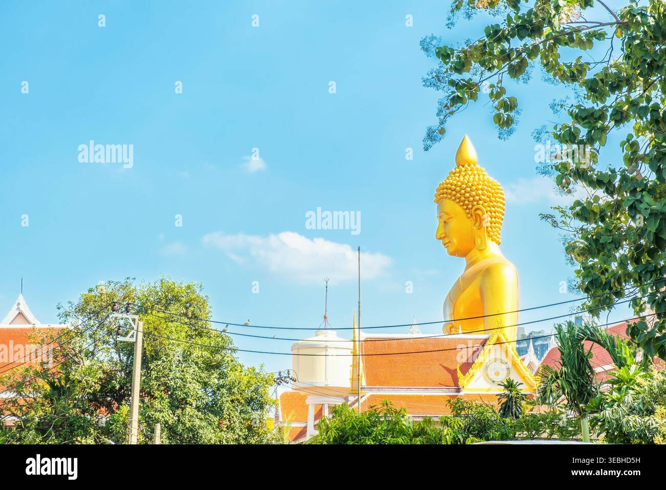 Vista laterale della gigantesca statua dorata del Buddha al Wat Paknam Phasi Charoen con tetti dei templi e alberi nella città di Bangkok, Thailandia. Grande Buddha seduto Foto Stock