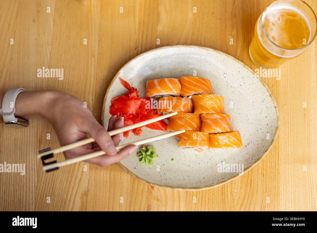 Sushi roll al salmone con birra. Vista dall'alto di sushi al salmone con bacchette, zenzero sottaceto, wasabi e un bicchiere di birra su un tavolo di legno. Foto Stock