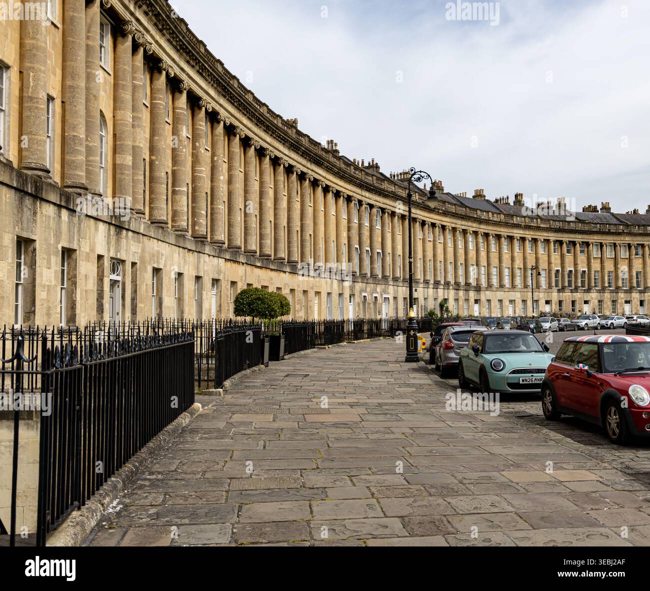 Il Royal Crescent di Bath, Inghilterra, presenta l'iconica architettura georgiana con una facciata curva in pietra e vista sulla strada con auto parcheggiate Foto Stock
