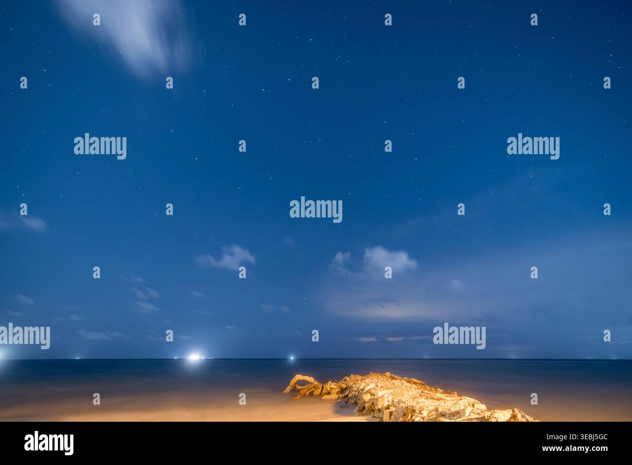 Stelle notturne sull'oceano calmo e sulla costa rocciosa Foto Stock