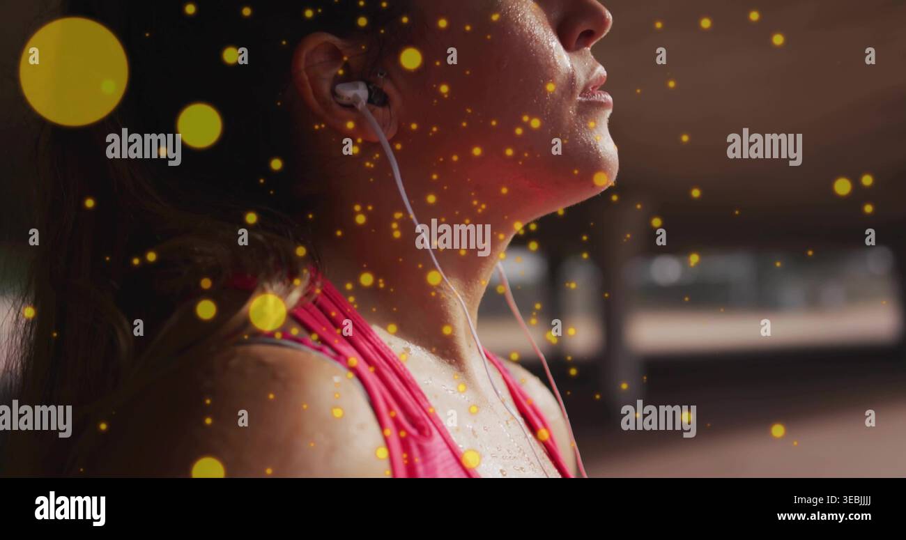 Donna ascoltatrice che indossa una canotta sportiva rosa nel parcheggio, con cavo auricolare cablato, sudore, bokeh giallo Foto Stock