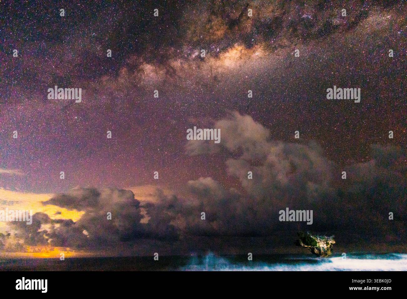 Un'affascinante scena notturna presenta un cielo stellato con la via Lattea. Un robusto foro sulla sinistra incornicia il paesaggio marino. Foto Stock