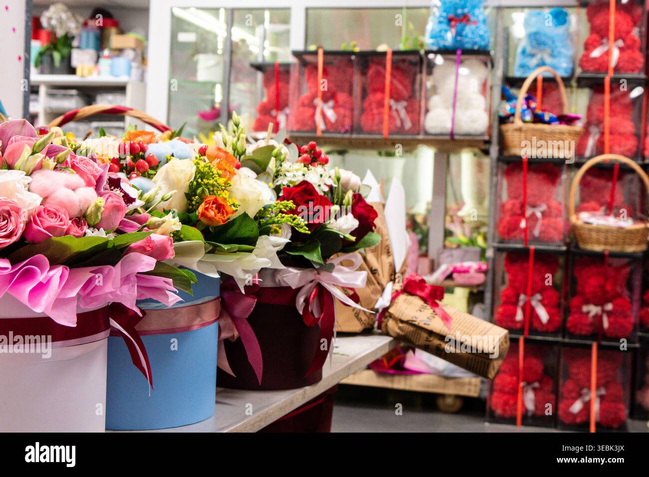 I colori ricchi riempiono l'animata esposizione di un negozio floreale. I fiori rosa, rosso e bianco emanano freschezza e gioia. I cestelli artigianali e i pacchetti confezionati aggiungono il cha Foto Stock