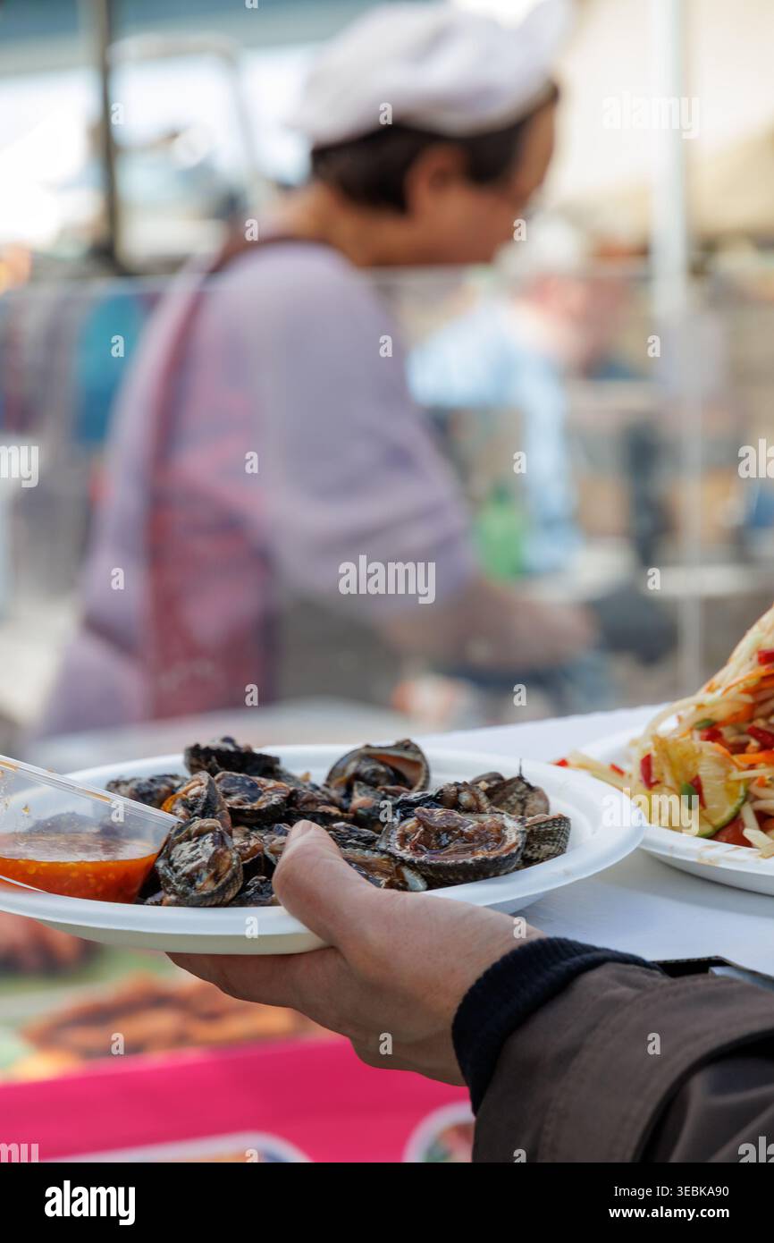 Vivace mercato all'aperto con snack di pesce serviti su vassoio monouso con condimenti Foto Stock