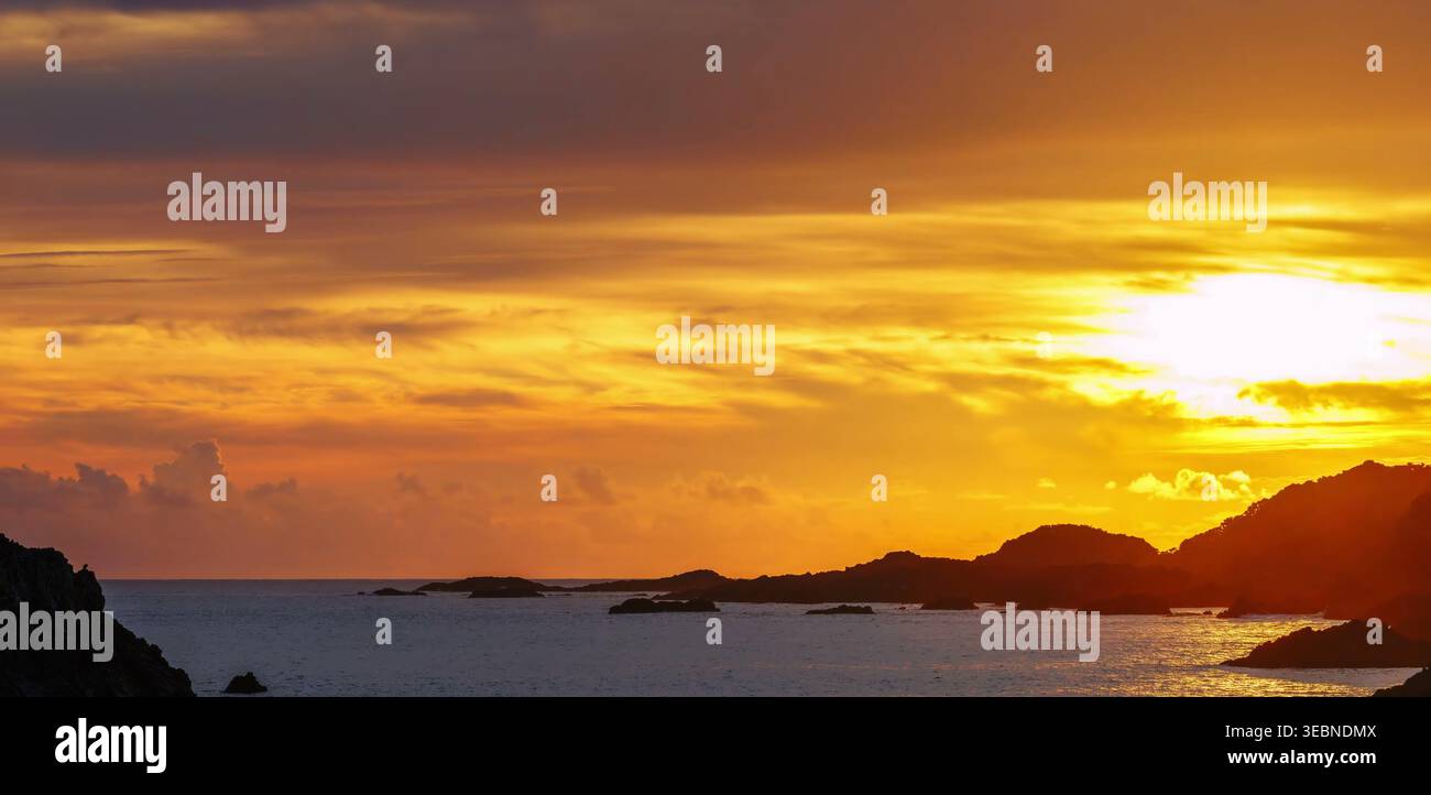 Il tramonto dorato risplende sulle linee scure della costa e sulle calme acque dell'oceano Foto Stock