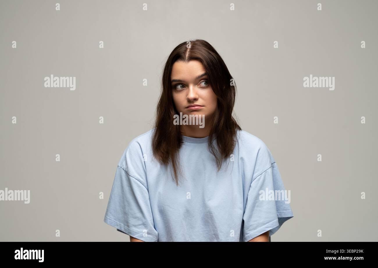 Giovane donna che guarda via con un'espressione scettica. Le labbra in posa mostrano noia e dubbio, catturando sentimenti di sospetto Foto Stock