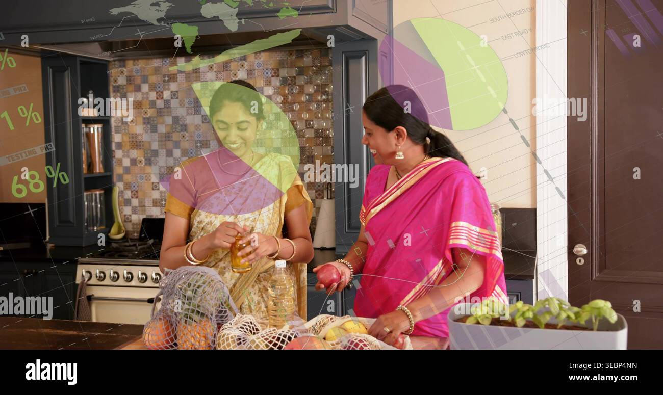 Preparare due donne indiane in sari dorati e rosa maneggiando melograno a Kitchen Island, con barattolo Foto Stock