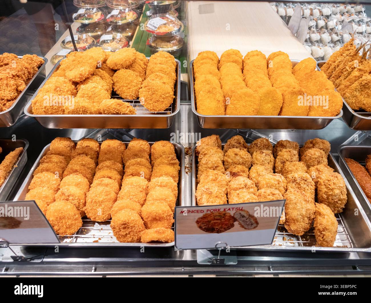 Vista ravvicinata delle crocchette impanate fritte di colore marrone dorato disposte ordinatamente in un vassoio di metallo presso un supermercato o un banco di alimentari. Foto Stock