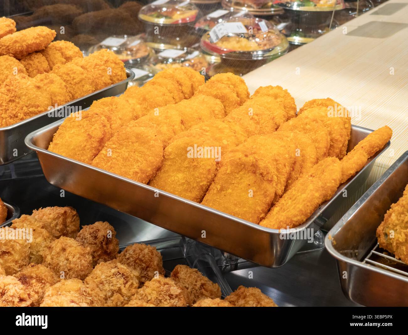 Vista ravvicinata delle crocchette impanate fritte di colore marrone dorato disposte ordinatamente in un vassoio di metallo presso un supermercato o un banco di alimentari. Foto Stock