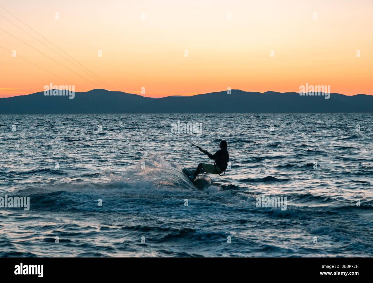Kitesurfer cavalca le onde dell'oceano sotto un bellissimo cielo al tramonto e montagne lontane Foto Stock